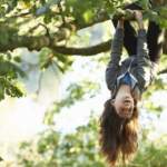Young girl hanging upside down branch